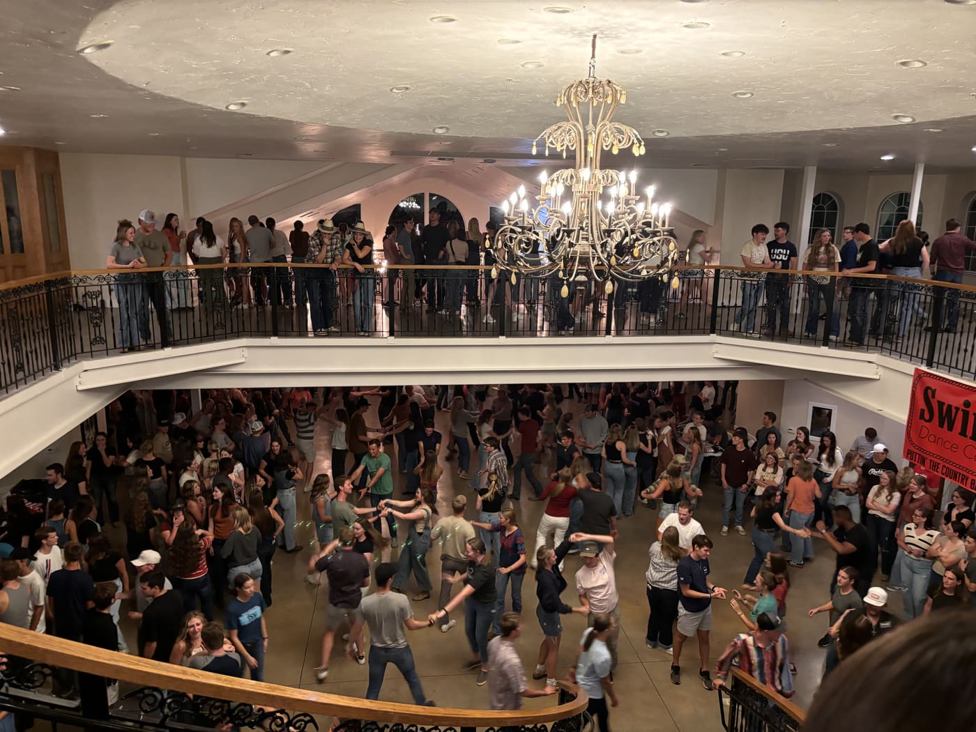 Dancers on the floor and spectators on the balcony at a packed Swingin Dance Co night